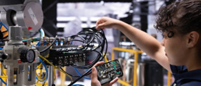A man looking at the mobile screen while holding some wires.