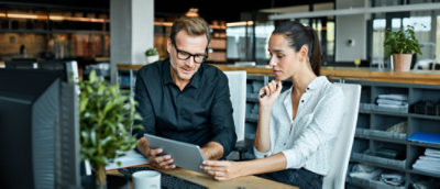 A man and a woman viewing a tablet at work.