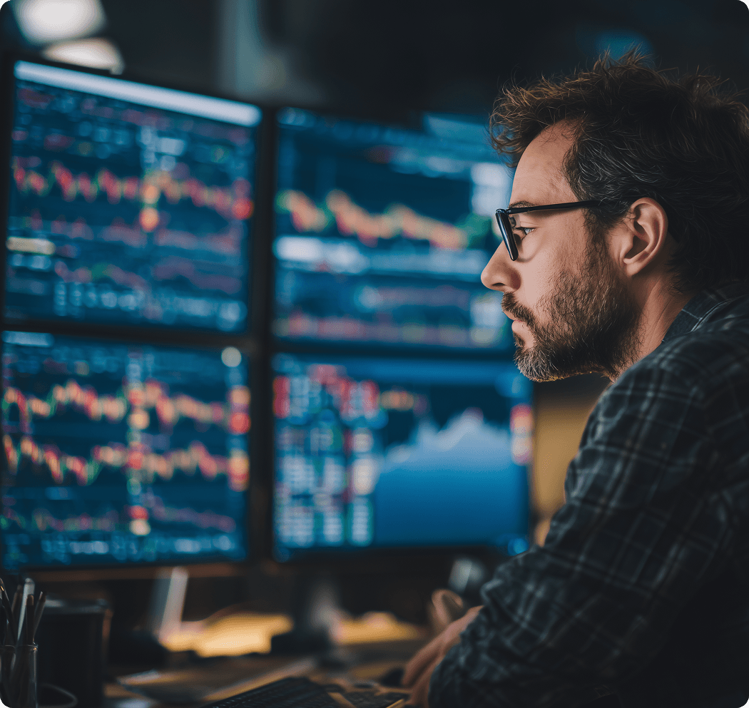 Man analyzing multiple data charts on computer monitors in a dark office, representing data monitoring, anomaly detection, and analytical focus.